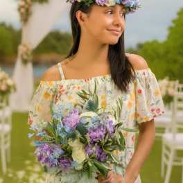 Woman holding a purple, blue, and white bouquet and wearing a matching floral crown outdoors