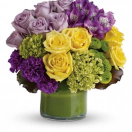 Bouquet of yellow, lavender, and purple flowers in a green glass vase