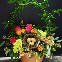 Floral arrangement with roses and hydrangea in a pot, topped with a bird nest and eggs