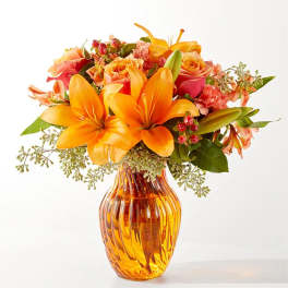 Orange lilies and roses arranged in an amber glass vase