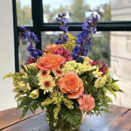 Mixed bouquet of orange, purple, and yellow flowers in a glass vase