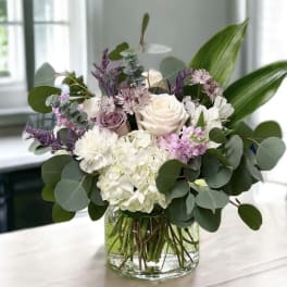 Mixed bouquet of white, blush, and purple flowers in a glass vase