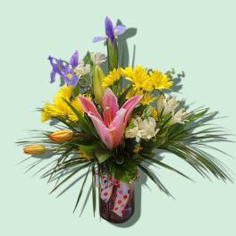Bouquet of pink lilies, yellow daisies, and purple irises in a glass vase