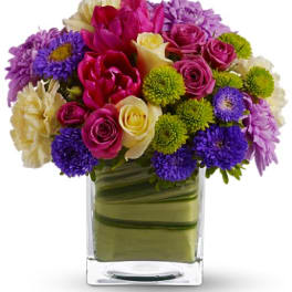 Mixed bouquet of pink, purple, yellow, and white flowers in a glass vase