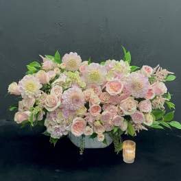Low pastel floral centerpiece in a white bowl with a candle beside it