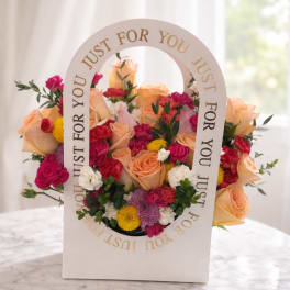 Mixed bouquet of peach roses, pink blooms, and yellow flowers in a white gift box