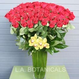Tall bouquet of red roses with yellow orchids in a glass vase