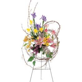 Tall floral standing arrangement with lilies, irises, and yellow blooms on a wire easel