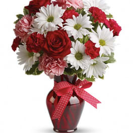 Red, pink, and white flowers arranged in a red vase with a polka-dot ribbon