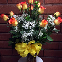 Yellow and red roses in a glass vase with baby's breath and a yellow ribbon