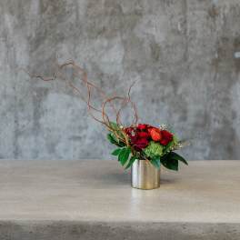 Red and orange floral arrangement in a metal vase with curly branches