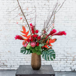 Tall tropical floral arrangement in a brown vase with red and orange blooms