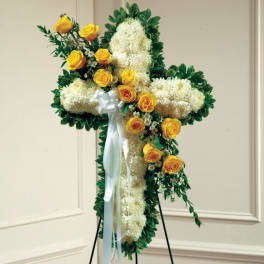 Floral cross arrangement with yellow roses and white blooms on a stand