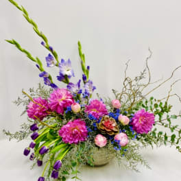 Bright mixed flower arrangement in a low bowl with pink, purple, and blue blooms