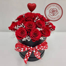 Round black box of red roses with white filler flowers and a red heart pick.