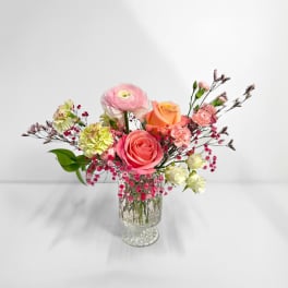 Mixed pink and peach flowers arranged in a clear glass vase