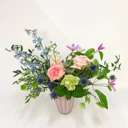 Loose arrangement of pink roses, blue delphinium, and green hydrangea in a pink vase