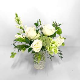 White roses arranged in a clear glass vase with green accents