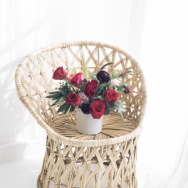 Red rose arrangement in a white vase on a wicker chair