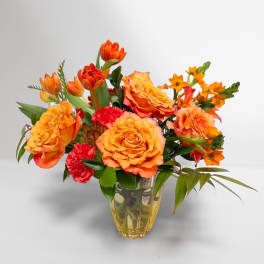 Orange roses and tulips arranged in a clear glass vase