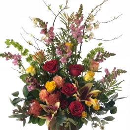 Tall mixed flower arrangement in a wooden container with red and yellow roses