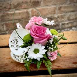 Pink rose and white daisy arrangement in a teacup with a handle