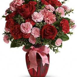 Red roses and pink carnations arranged in a red vase with a pink ribbon