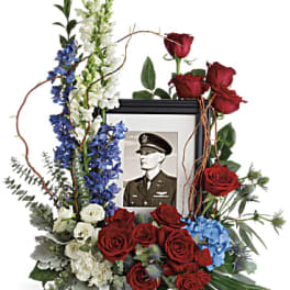 Floral tribute around a framed portrait with red roses and blue and white blooms