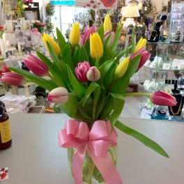 Bouquet of pink and yellow tulips in a glass vase with a pink ribbon