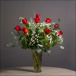Red roses arranged in a clear glass vase with white filler flowers