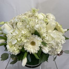 White floral arrangement in a glass vase with hydrangeas, roses, and daisies