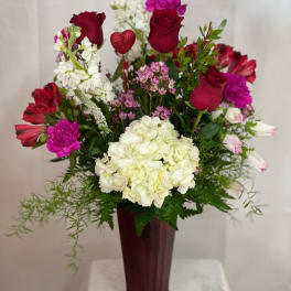 Mixed bouquet of red roses, white hydrangea, and pink flowers in a tall vase