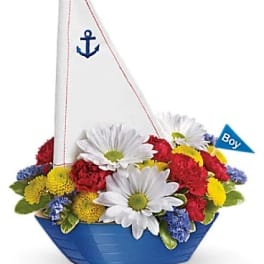 Flower arrangement in a blue sailboat container with a white sail