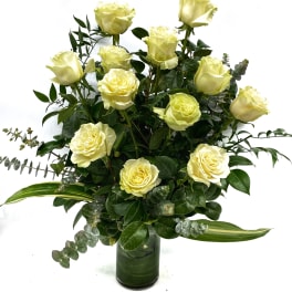Yellow roses arranged in a glass vase with eucalyptus and greenery