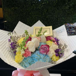 Colorful bouquet of roses, hydrangeas, and carnations wrapped in white paper with a pink bow