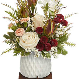 White roses and burgundy flowers in a white vase on a wooden stand
