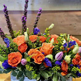 Orange roses and purple flowers in a low rectangular arrangement
