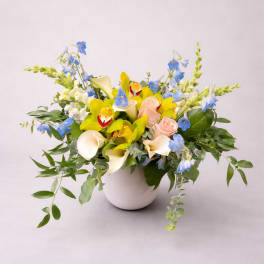 Mixed bouquet in a white vase with yellow, blue, peach, and white flowers
