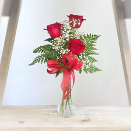 Three red roses in a clear glass vase with baby's breath and a red ribbon