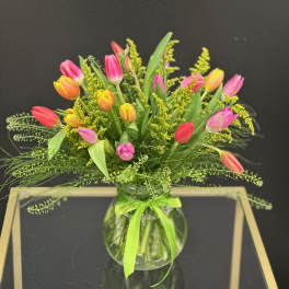 Colorful tulip bouquet in a round glass vase with a green ribbon