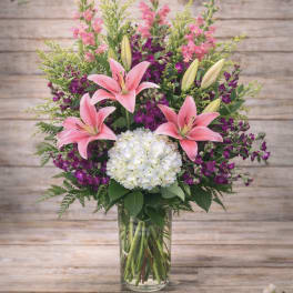 Pink lilies and purple flowers arranged in a glass vase with white hydrangea