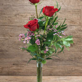 Three red roses in a clear glass vase with pink filler flowers