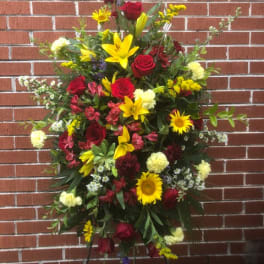 Standing floral spray with red roses, yellow lilies, and sunflowers
