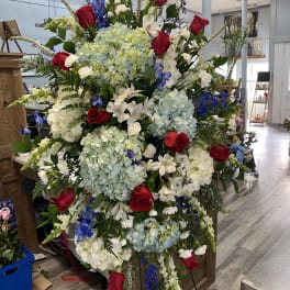 Large standing floral spray with red roses, blue hydrangeas, and white blooms