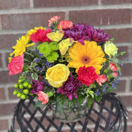 Colorful mixed bouquet in a clear glass vase with a butterfly pick