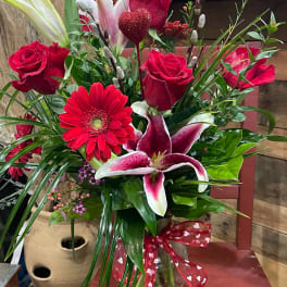Red roses and pink lilies in a glass vase with a heart ribbon