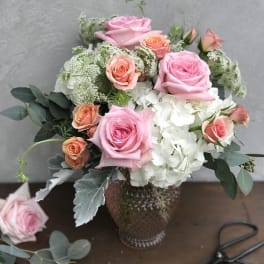 Pink and peach roses arranged with white hydrangea in a glass vase