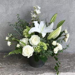 White roses and lilies arranged in a black vase with green accents