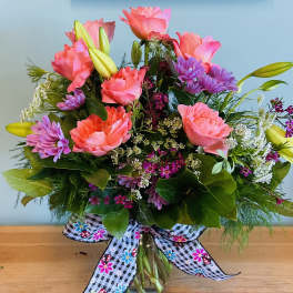 Pink roses and purple daisies in a glass vase with a patterned bow