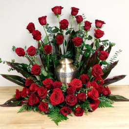 Red roses arranged around a gold urn with greenery